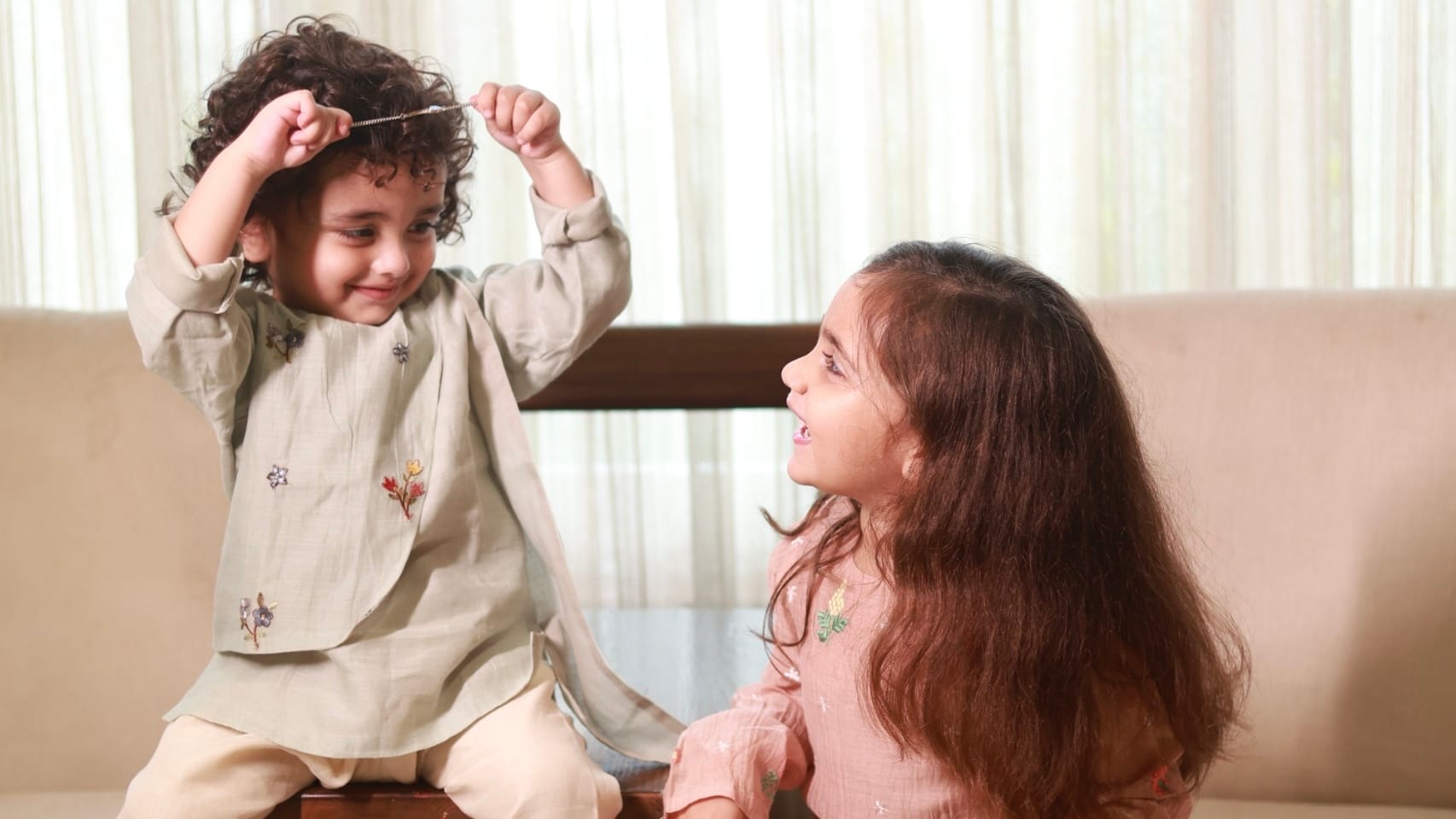 Two children in embroidered kachche dhaage kurta sets, sitting together on a low wooden table