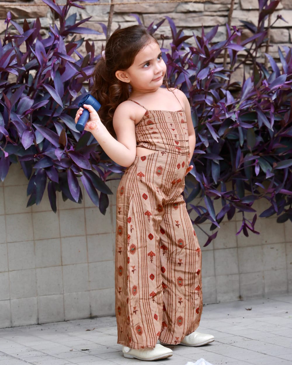 A girl in a tan block-printed jumpsuit with wide legs, against purple foliage