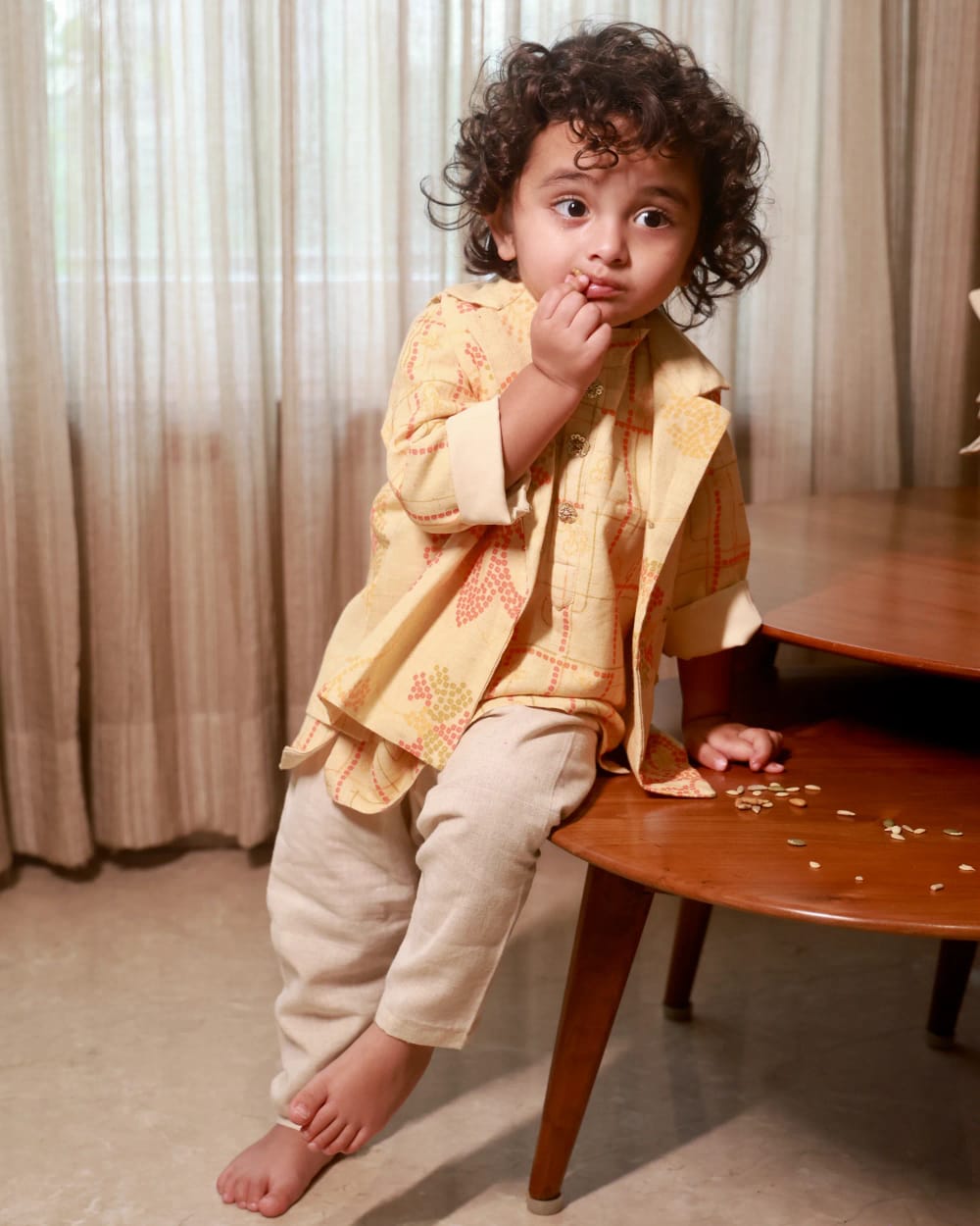 A child in a butter-yellow kurta printed in rust, worn open over a cream pyjama
