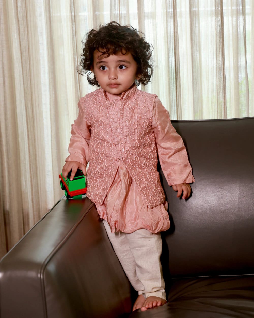 A child in the blush beaded kurta and cream pyjama, standing by a sofa