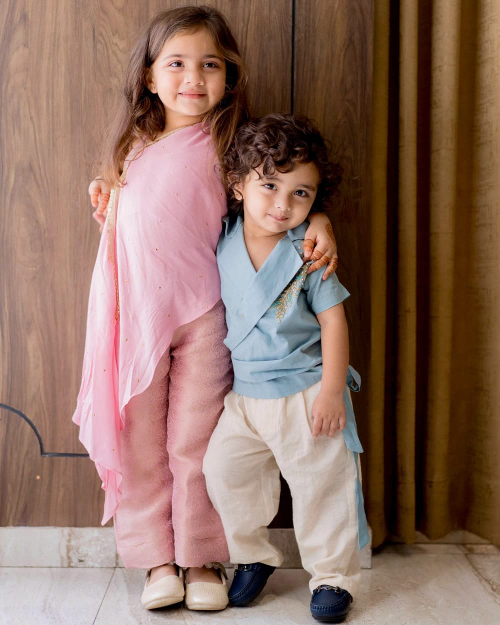Two children side by side, one in a pink cape top, the other in a teal wrap kurta