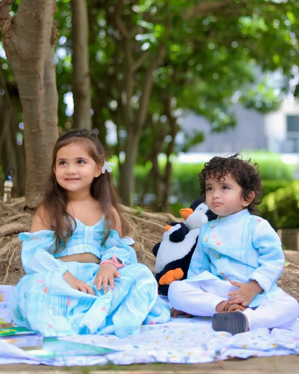 Two children sitting together on a blanket in matching pale blue