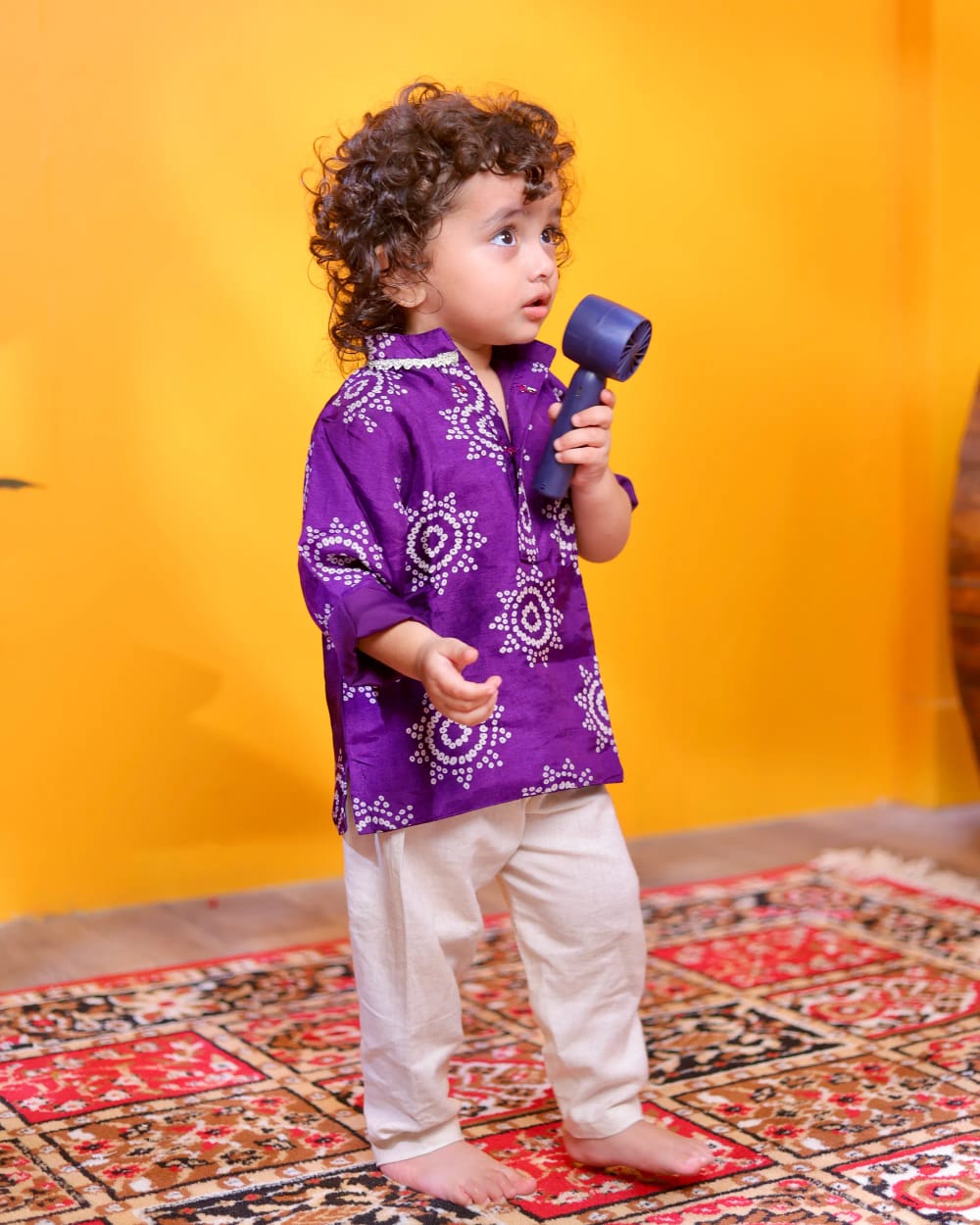 A boy in a purple bandhani kurta and cream pyjama