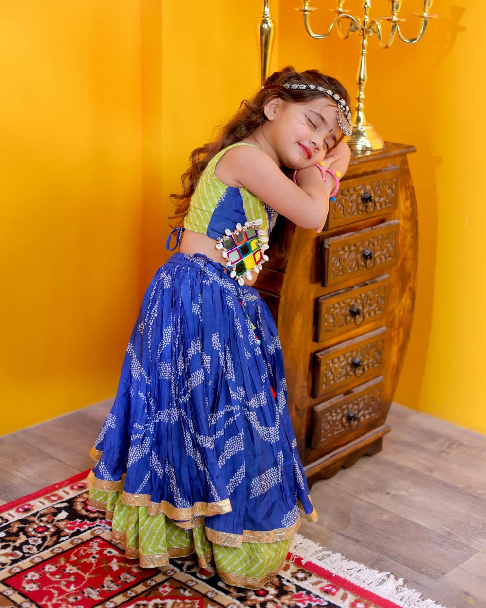 A girl leaning against a wooden chest in the blue bandhani ghagra