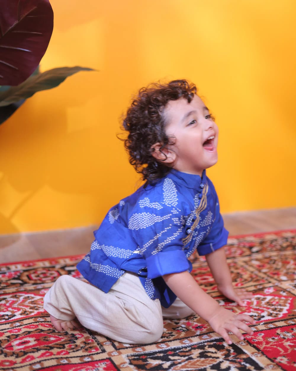 A boy sitting on the floor in the blue bandhani kurta, laughing