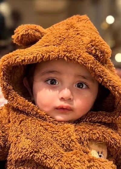 A baby in a hooded teddy-bear suit, sitting in a leather armchair