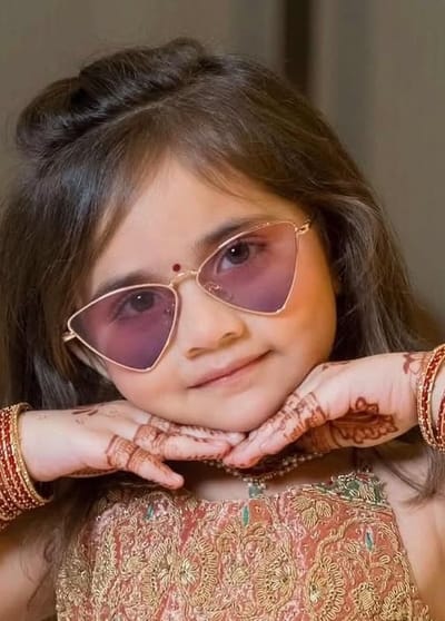 A girl in a maroon and gold lehenga and sunglasses, chin resting on her hands